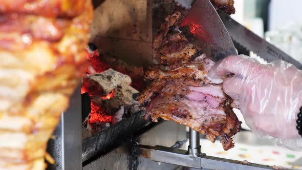 A cook cuts meat to make shawarma, gyros, doner kebab. Cooking meat on a skewer. Street food