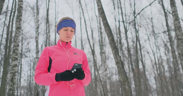 A Young Female on the Morning Jog Holds in Her Hands a Smartphone Picks a Music Track for Training alt
