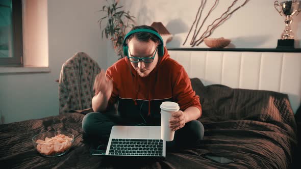 Young Man Sitting on the Bed and Talking with Somebody Using Laptop alt