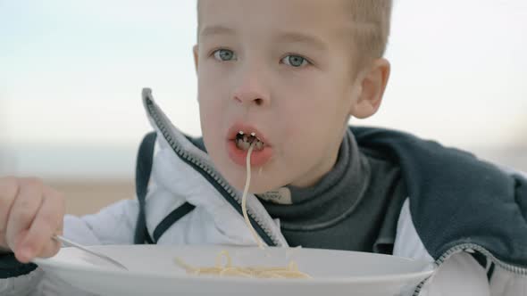Young boy eating pasta outside alt