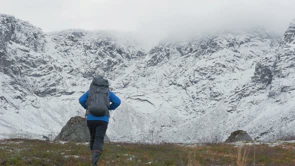 A Man with a Backpack Travels in the Mountains. He Looks at High Peaks and Goes Further