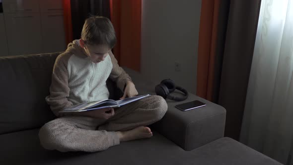Teen Boy Reads a Book Sitting on the Couch. Coronavirus Epidemic 2020.