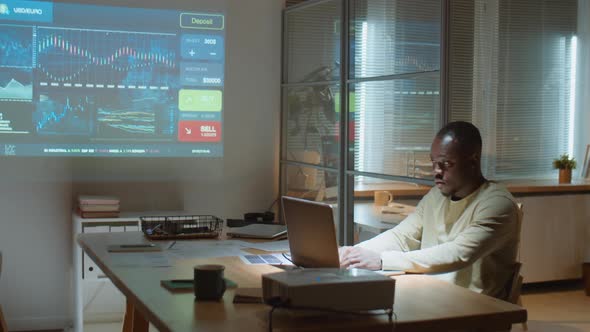 African American Trader Working on Laptop in Office at Night alt
