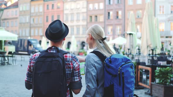 Back View of Tourists Couple with Bags Checking Map on Central City Square alt