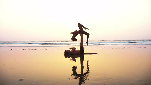 Fit Sporty Couple Practicing Acro Yoga with Partner Together on the Sandy Beach alt