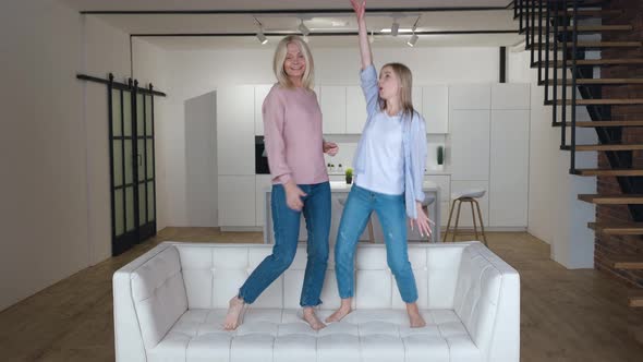 Happy Family Senior Mom Having Fun with Adult Daughter Dancing on Sofa in Living Room alt