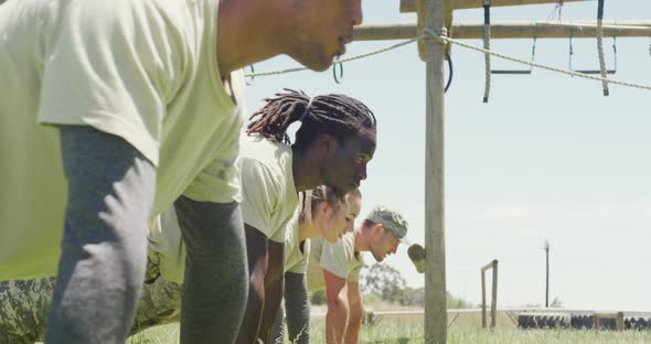 Diverse group of soldiers in doing doing plank exercise at army obstacle course in the sun alt