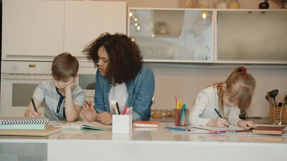 Serious Kids Boy and Girl Doing Homework with Caring Babysitter at Home alt