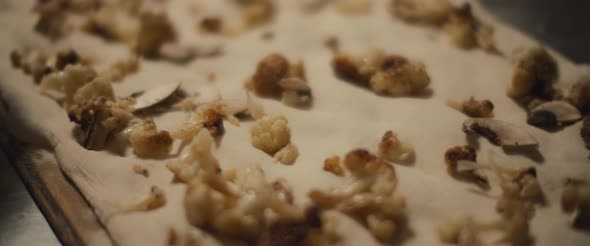 Fried cauliflower and mushroom toppings spread over fresh pizza dough, ready to be baked alt