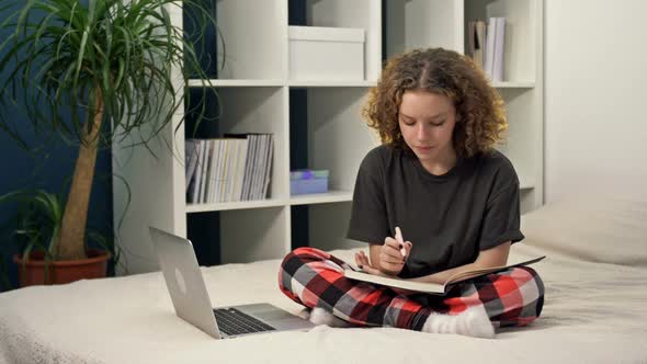 Cute Teenage Girl Doing Homework Sitting on the Bed at Home