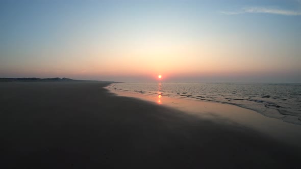 Aerial, drone shot low, waves at a beach, sunset in the background, on Langeoog island alt