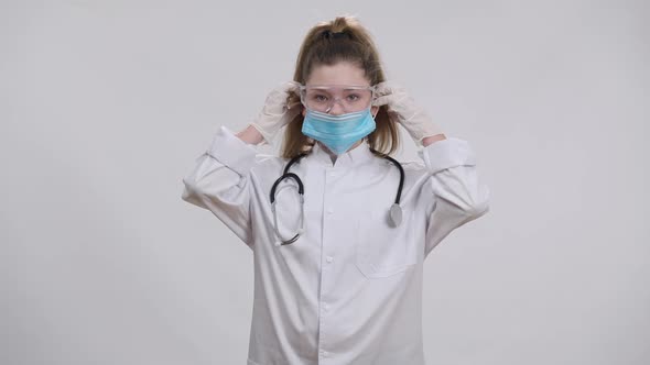 Little Caucasian Nurse Doctor Putting on Medical Covid19 Face Mask Looking at Camera alt