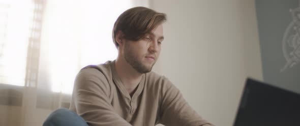 A close up of a young man sitting in bed and working on a computer.  alt