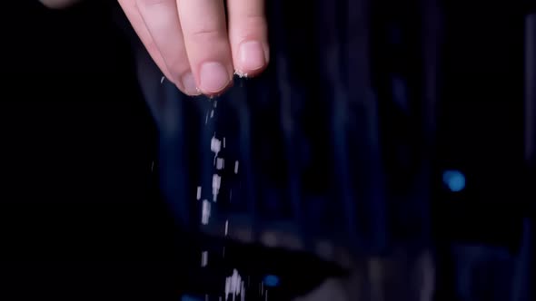 Male Fingers Over a Pot of Boiling Water Pouring Salt Into the Pan Closeup Dark Background alt