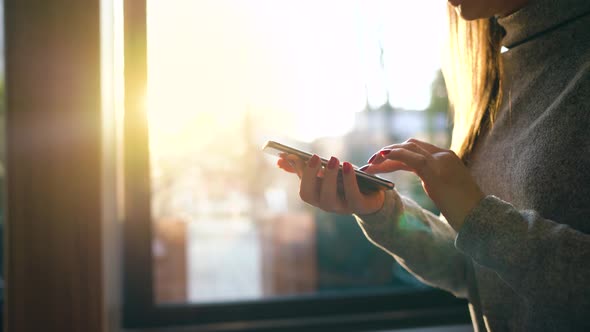 Female Hands Using Smartphone Against a Blurred Cityscape in the Setting Sun alt