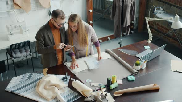 Tailors Male and Female Looking at Clothes Drawings and Using Smartphone Working in Studio Together alt