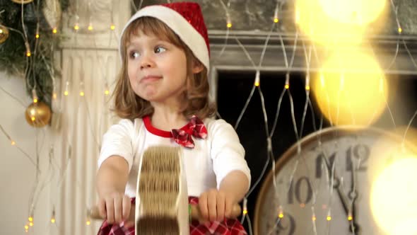 Child Rocks Wooden Rockinghorse on Background of Christmas Tree and Clock