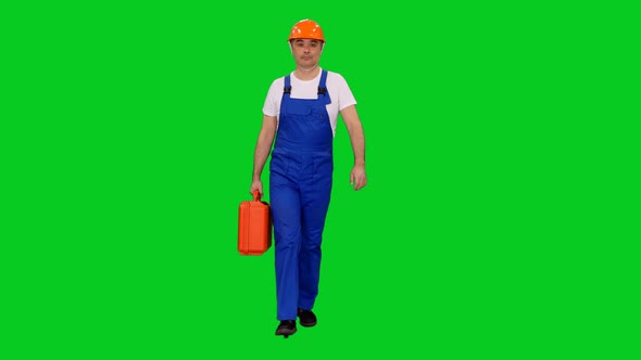 Confident Asian Builder In Blue Overalls And Hard Hat Walking With Red Suitcase