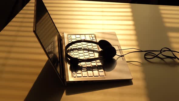 A Man Takes Headphones From the Keyboard of a Laptop in the Sunbeams of the Sunset alt