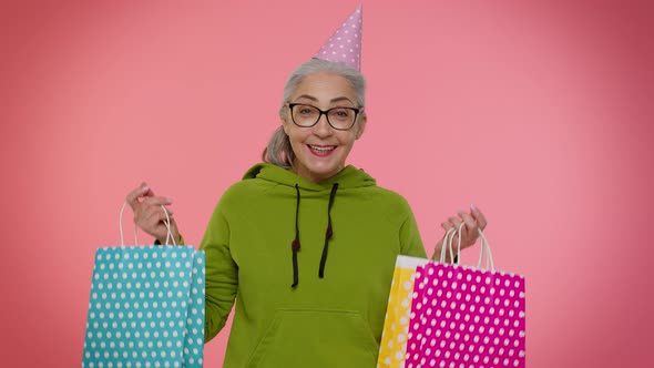 Elderly Granny Woman Showing Shopping Bags Advertising Discounts Looking Amazed with Low Prices alt