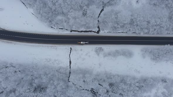 Aerial shot: a grader is cleaning the road of a snow in winter forest.