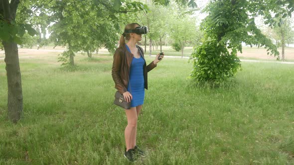Girl in a Virtual Reality Helmet Uses a Virtual App in the Park