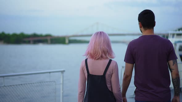 Live Camera Follows Millennial Caucasian Couple Walking on Urban Embankment to River Outdoors alt