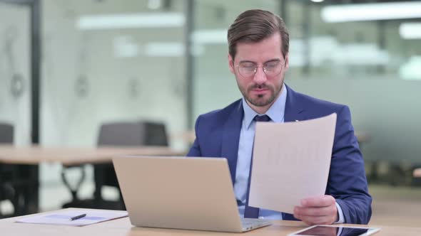 Serious Businessman Working on Laptop with Documents alt