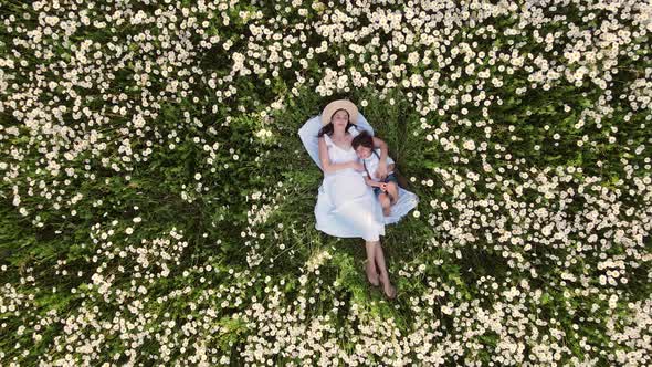 Beautiful Woman Mom in a White Dress and Hat with a Boy Son Lying on Her Back in a Field with alt