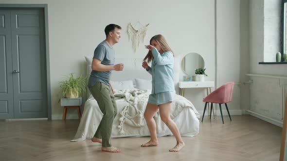 Cheerful Girl and Guy Dancing in Bedroom at Home Having Fun in Apartment alt