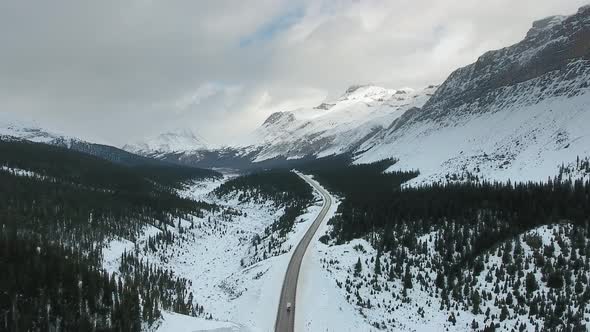 Drone footage of car moving along the road surrounded by snowy mountains in Alberta, Canada alt