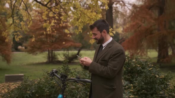 Handsome young man with electric bicycle using mobile phone in the autumn park