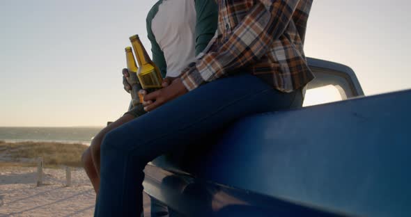 Couple with beer bottles sitting on pickup truck at beach 4k alt