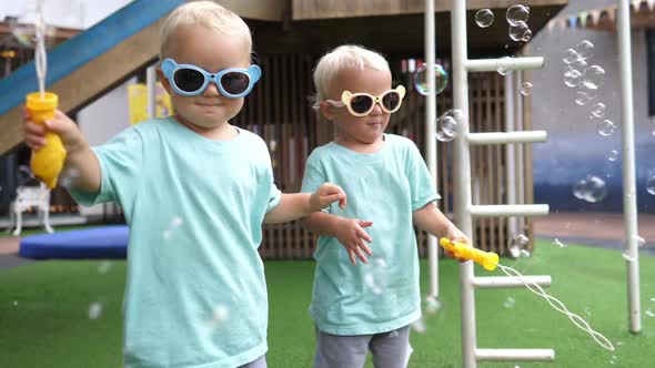Cute Twin Girls Wearing Colourful Sunglasses Playing with Soap Bubbles alt