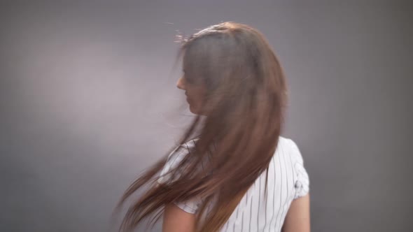 Portrait of adorable lady making long hair flyaway and turns on grey background alt