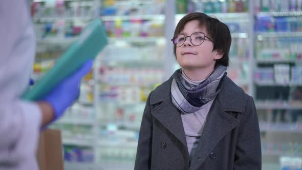 Portrait of Confident Cute Boy Receiving Shopping Bag with Pills From Pharmacist Thanking Walking alt