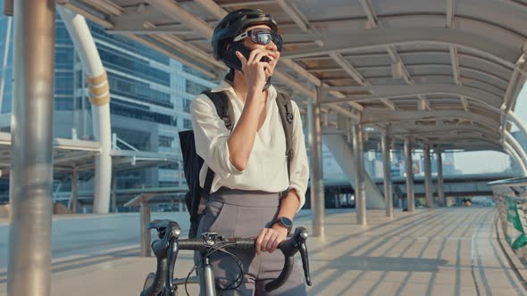 Asian businesswoman with backpack pick up mobilephone talk smiling watch smartwatch in city. alt