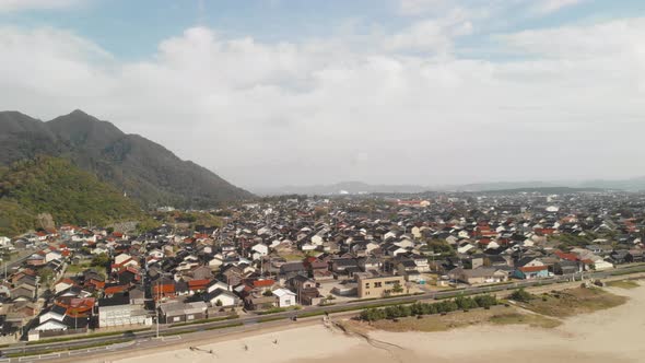 Right Aerial Drone pan over Japanese coastal city with mountains on bright day alt