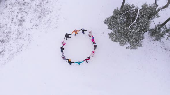 Aerial view group men and women during day in winter snowy forest in round dance