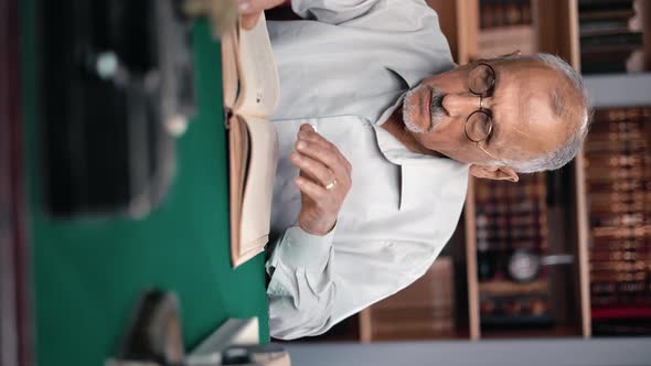 VERTICAL VIDEO POV Sad 70s Grandfather Reading Book Sitting at Table in Vintage Public Library alt