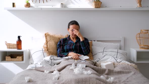 Sick Woman Looks at Thermometer and Blows Nose alt