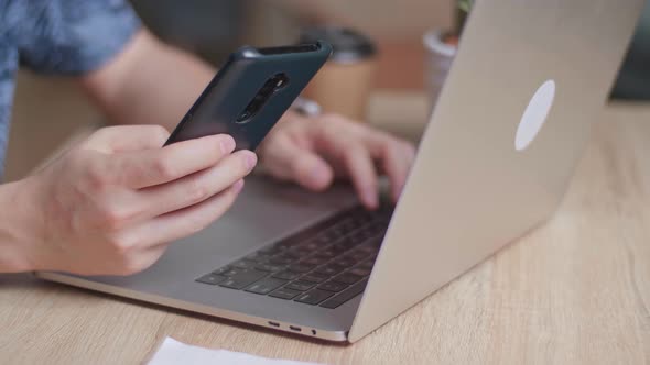 Hands Man Using Mobile Phone During Work On Laptop Computer alt