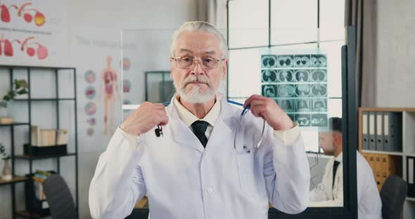 Doctor Putting on His Stethoscope Around His Neck Looking Into Camera in Modern Hospital Office alt