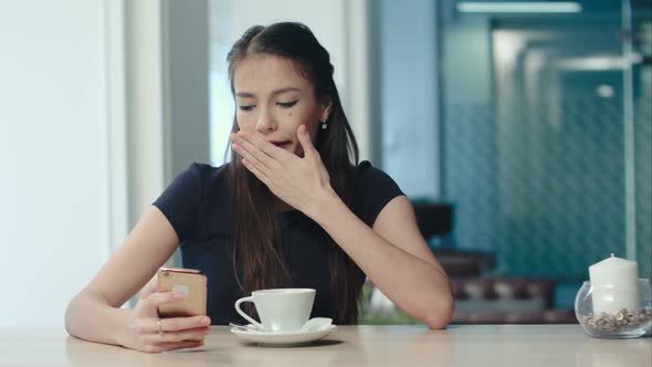 Young Bored Brunette Yawning and Stretching and Drinking Coffee in a Cafe alt