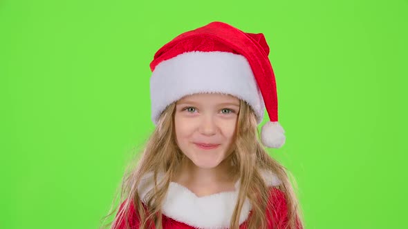 Child Girl in a Beautiful Suit and a Red New Year's Cap Smiles. Green Screen alt