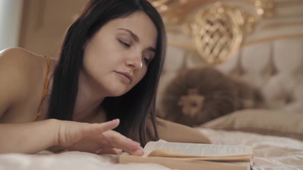 Beautiful Caucasian Woman Lying on the Bed and Reading a Book