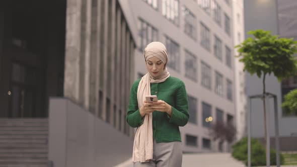 Arabian Business Woman in Hijab Using Smartphone While Standing Outdoors Near Office Building alt