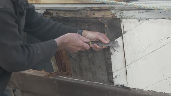 Carpenter scrapes off paint to locate screws on wooden boat Seaplane Tender restoration alt
