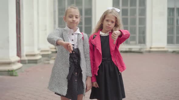 Portrait of Two Dissatisfied Schoolgirls Showing Thumbs Down. Cute Unhappy Caucasian Girls Unwilling alt