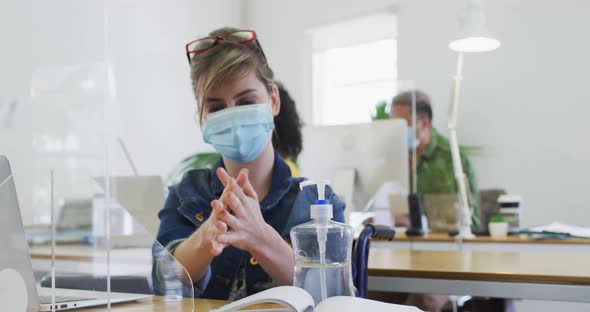 Woman wearing face mask sanitizing her hands at office alt
